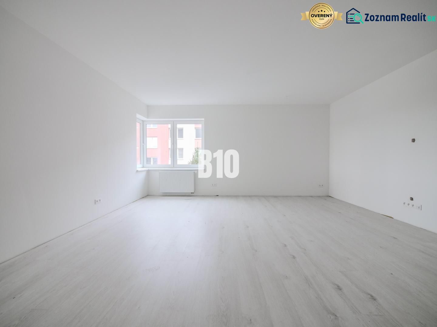 A spacious room in a one-bedroom apartment with a wood-decor floor and a large window.