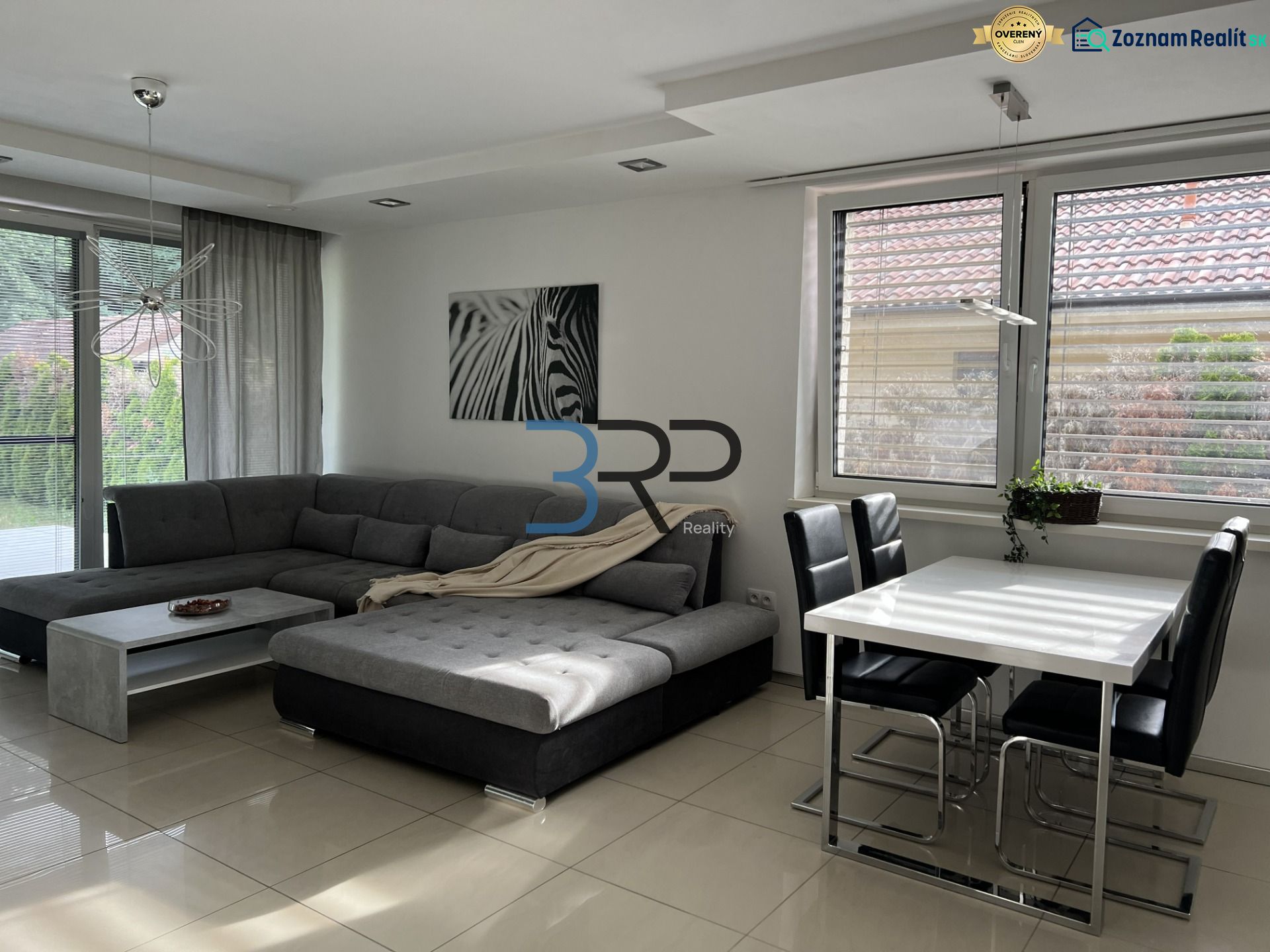 Living room of a family house with a corner sofa, a zebra poster, and a dining table.