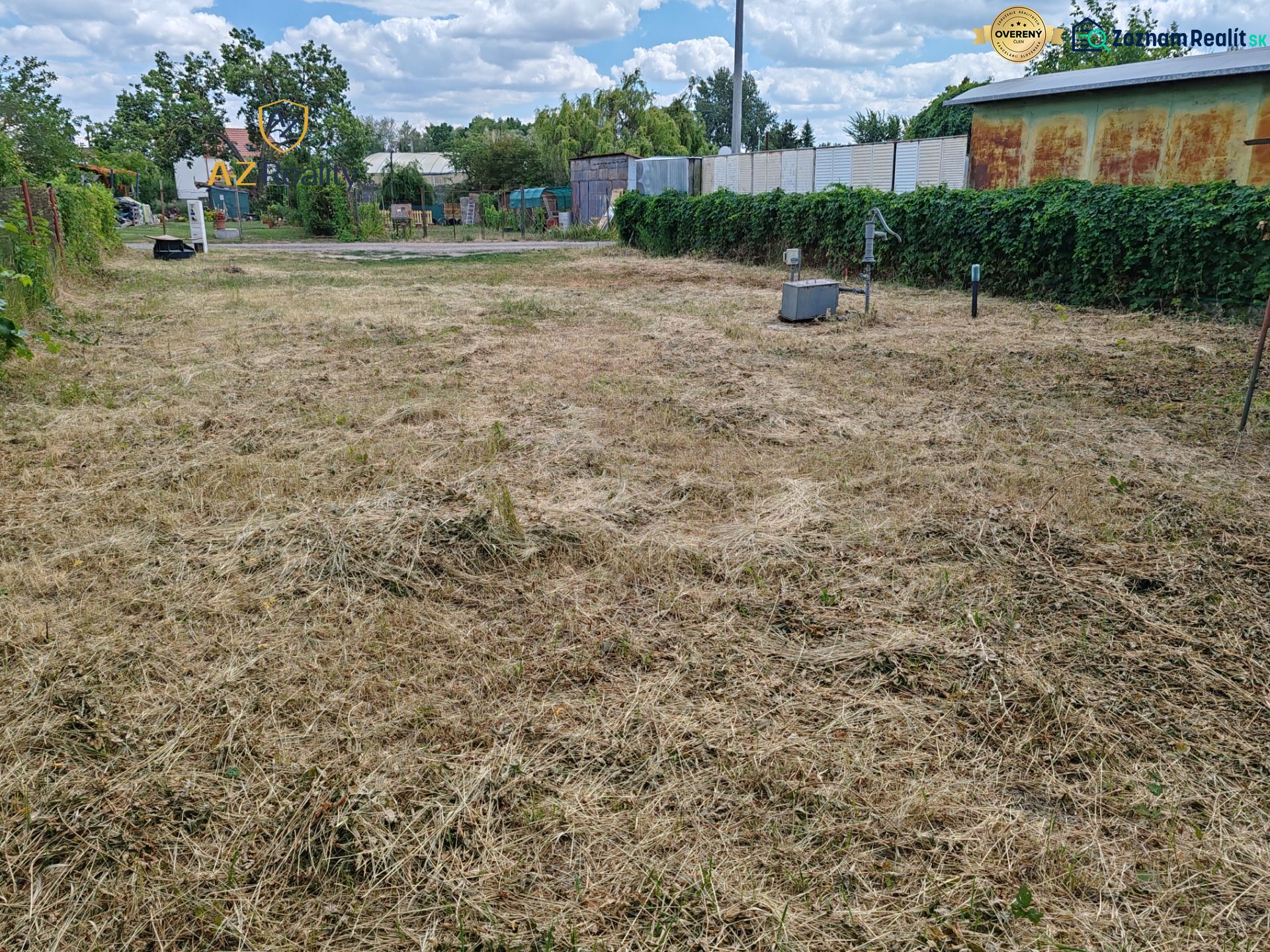 The grassy area in the gardens of Komárno, bordered by a fence and landscaped vegetation.