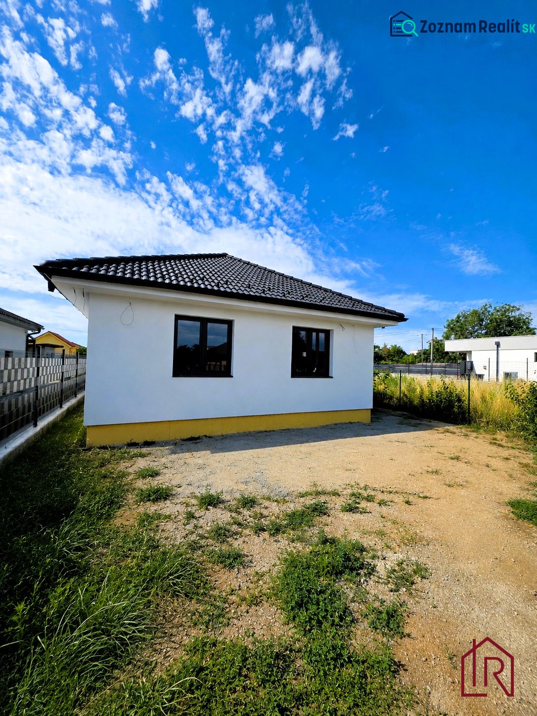 A family house in Čaňa with a white facade and a sloped roof under a blue sky.