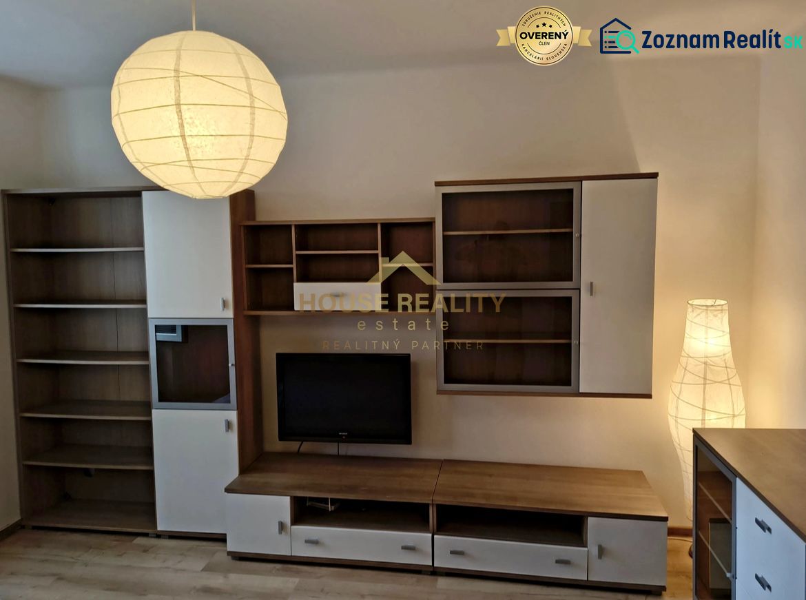 Living room in a studio apartment with furniture and a television on a wooden floor.