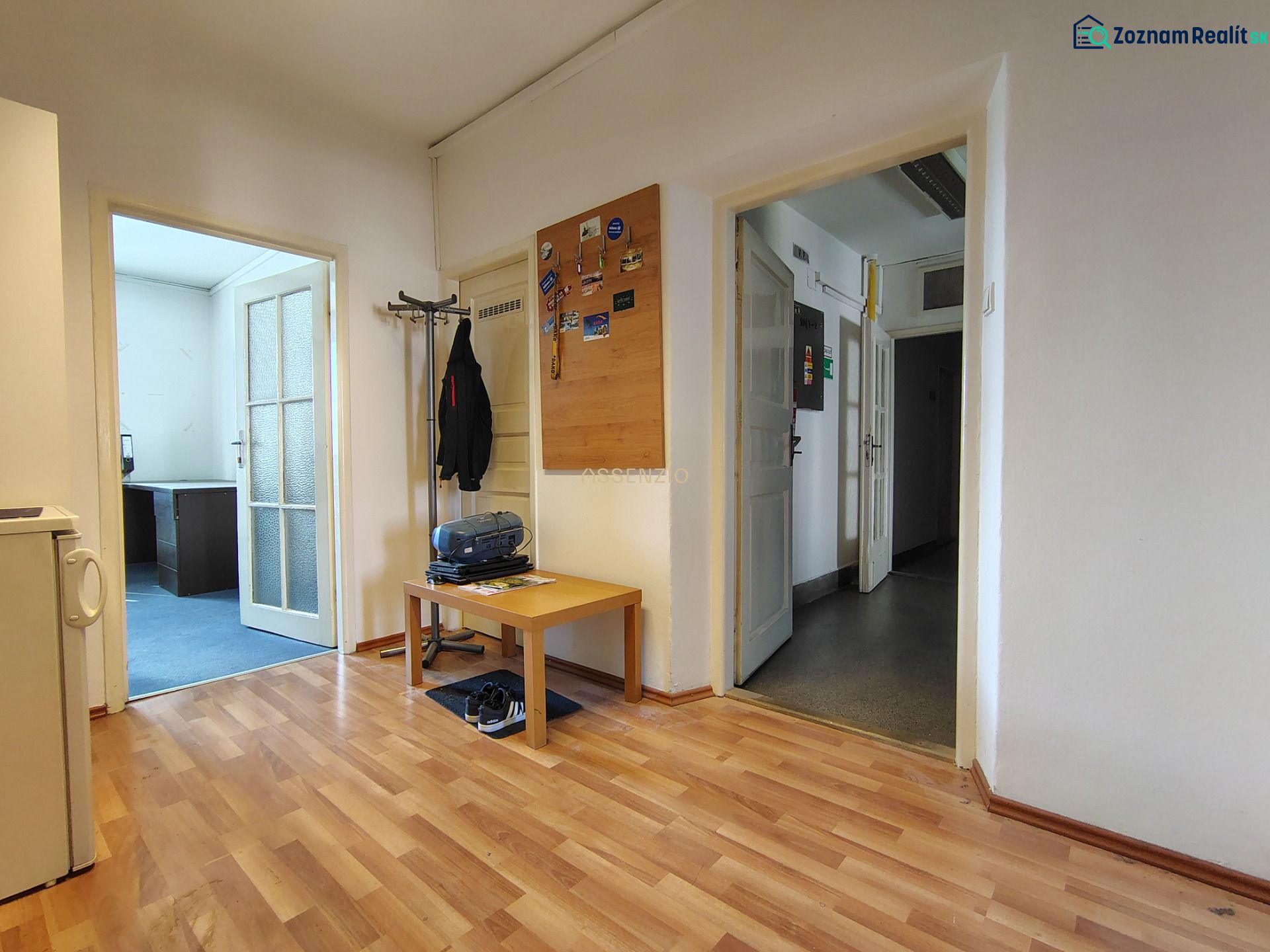 Offices with wood-patterned flooring, a coat rack, a table, and adjacent rooms.