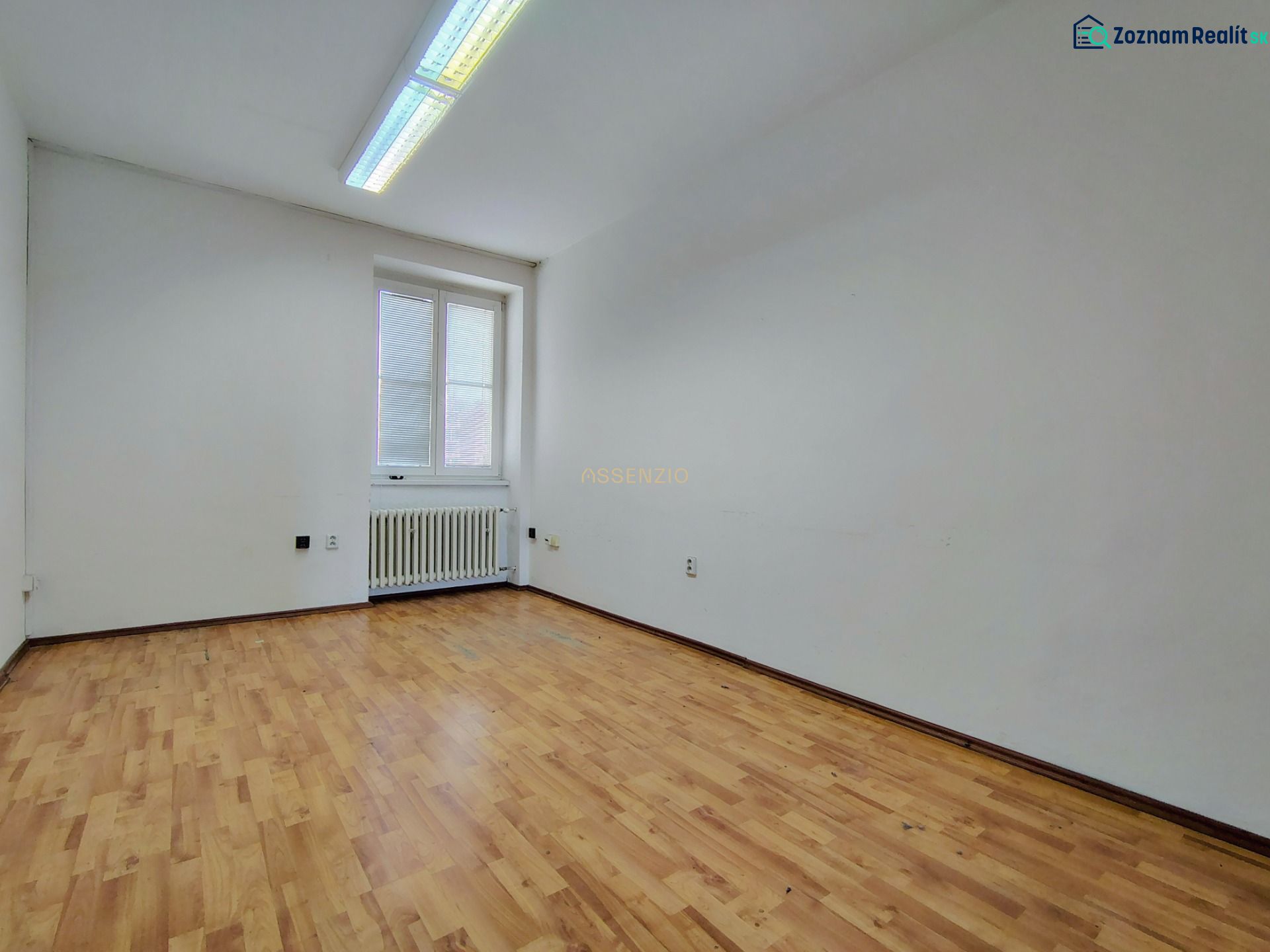 An empty office with a wooden floor and a radiator under the window.