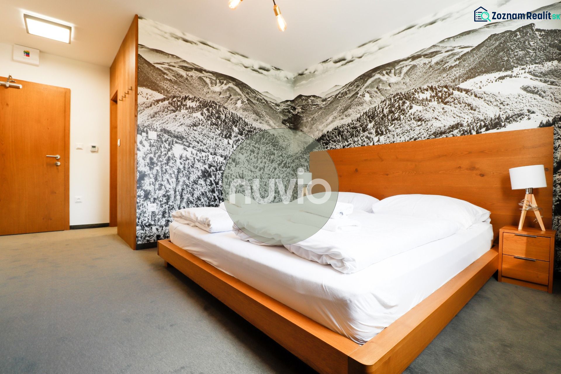 A bedroom in a holiday apartment with a wooden bed and a mountain photo wallpaper.