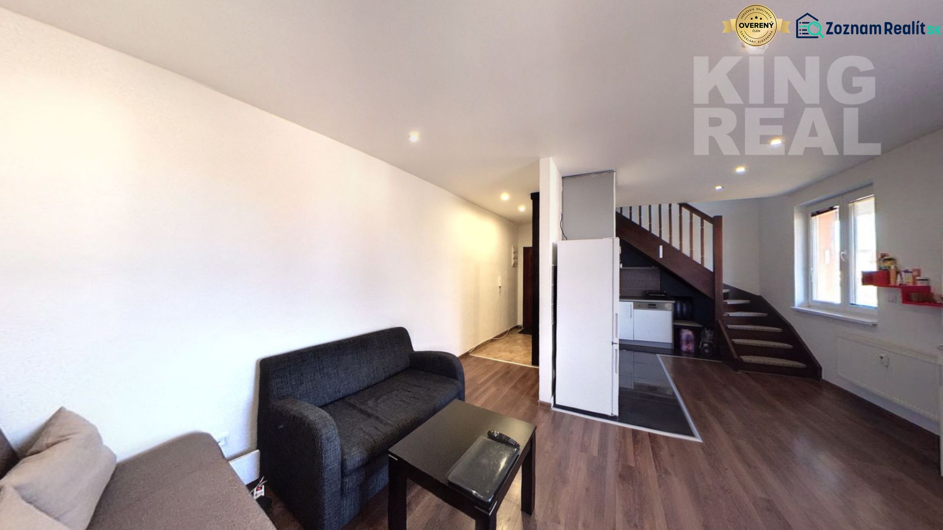 Living room of a 2-room apartment with a sofa, a table, and a staircase. Floor with wood decor.