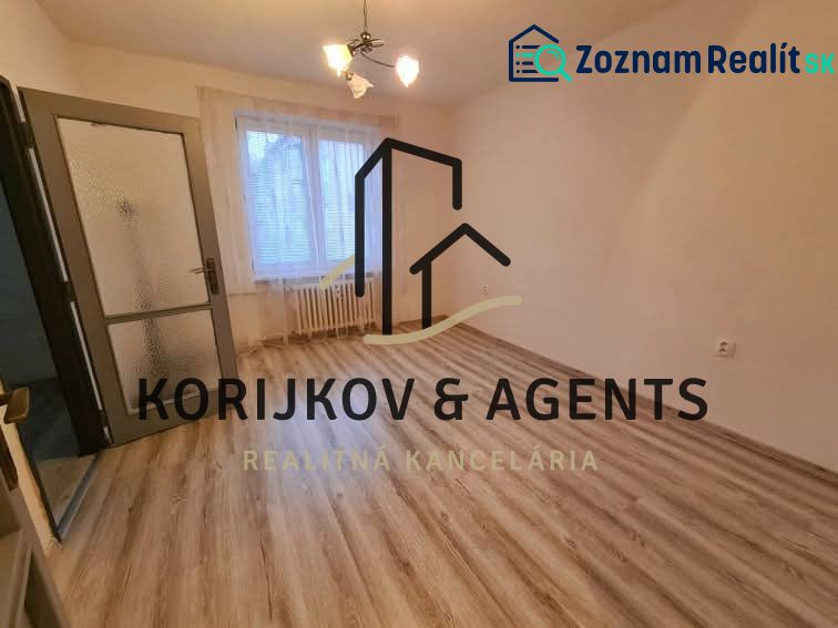 A room in a 2-room apartment with a wooden decor floor and a window with a blind.