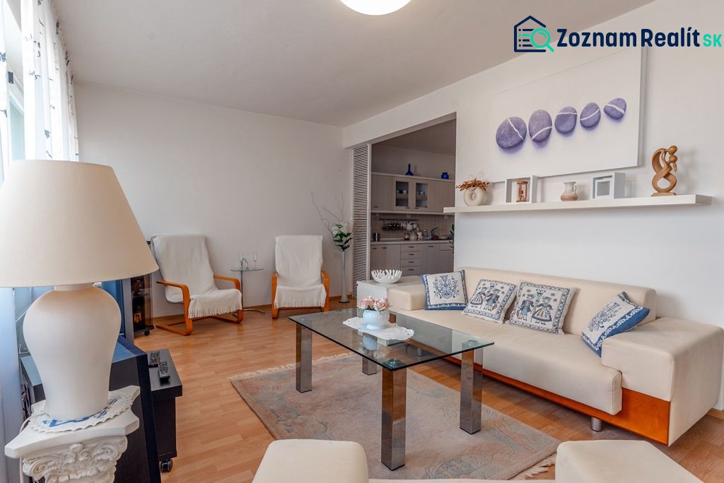 Living room with a sofa, glass table, and wooden decor flooring in a three-room apartment.