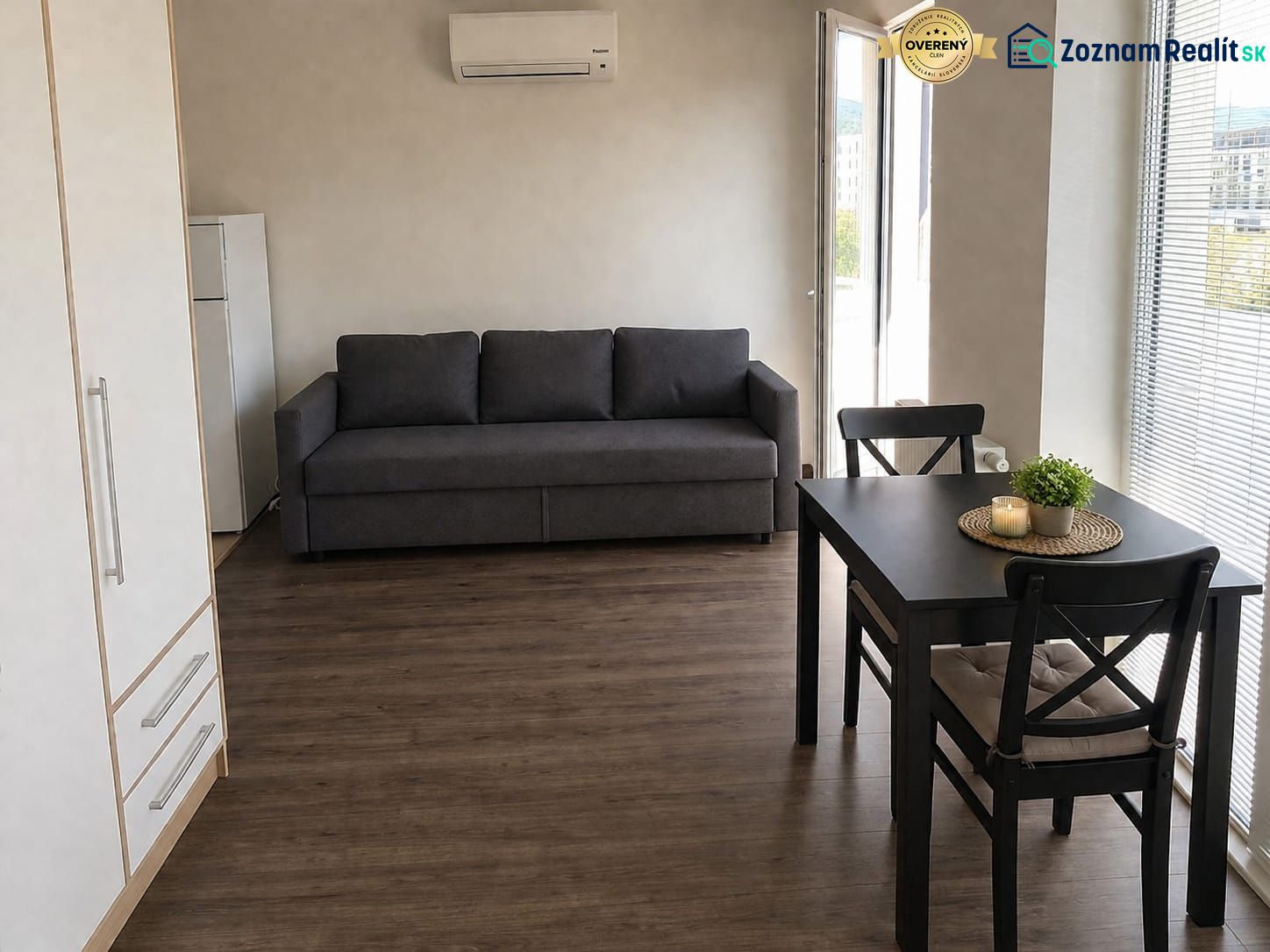 Living room in a studio apartment with wood-patterned flooring, a sofa, and a dining table.