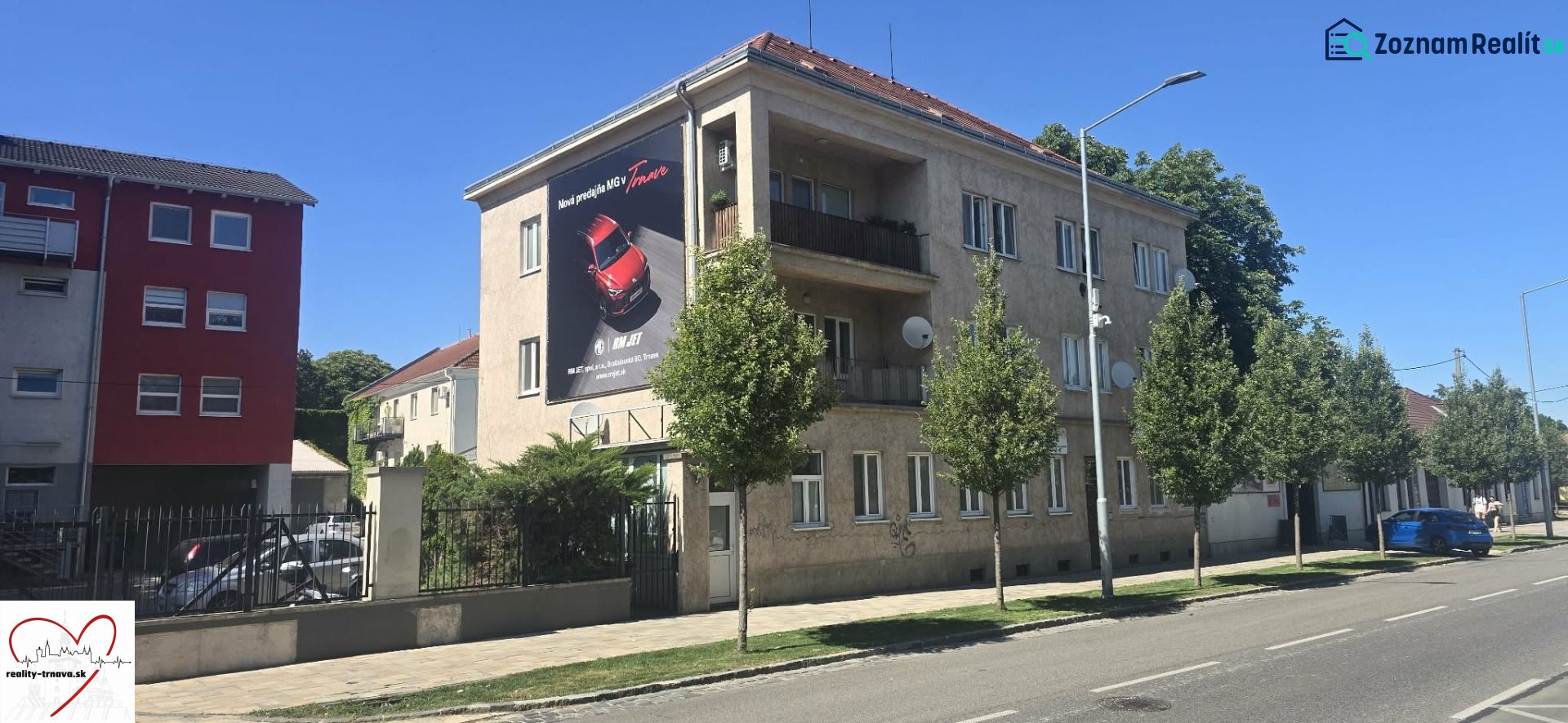 A building with an advertisement in Trnava on Zelený kríček, with parked cars next to it.