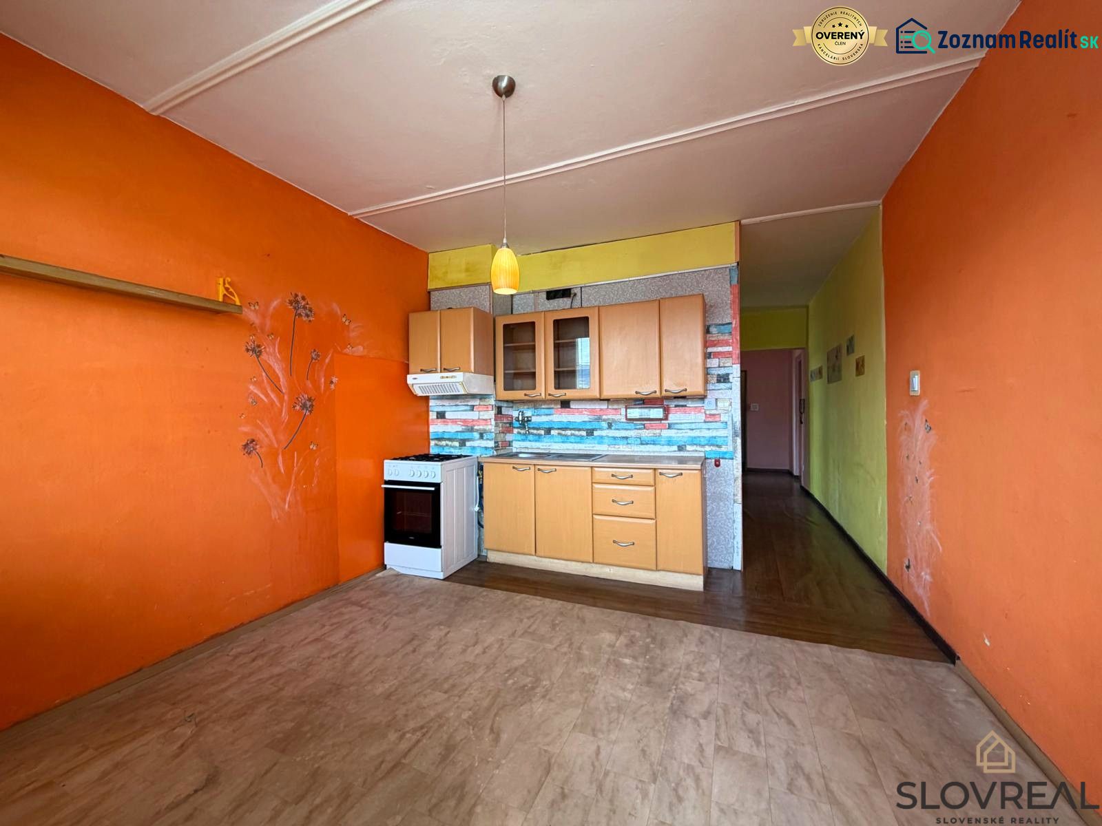 A kitchen in a 3-room apartment with a wooden decor floor and an orange wall.