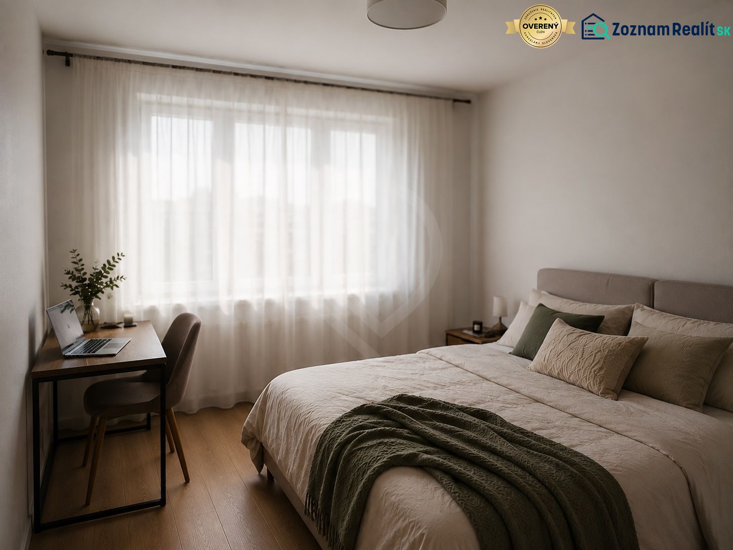 A bright bedroom in a two-room apartment with a wood-patterned floor, a desk, and a double bed.
