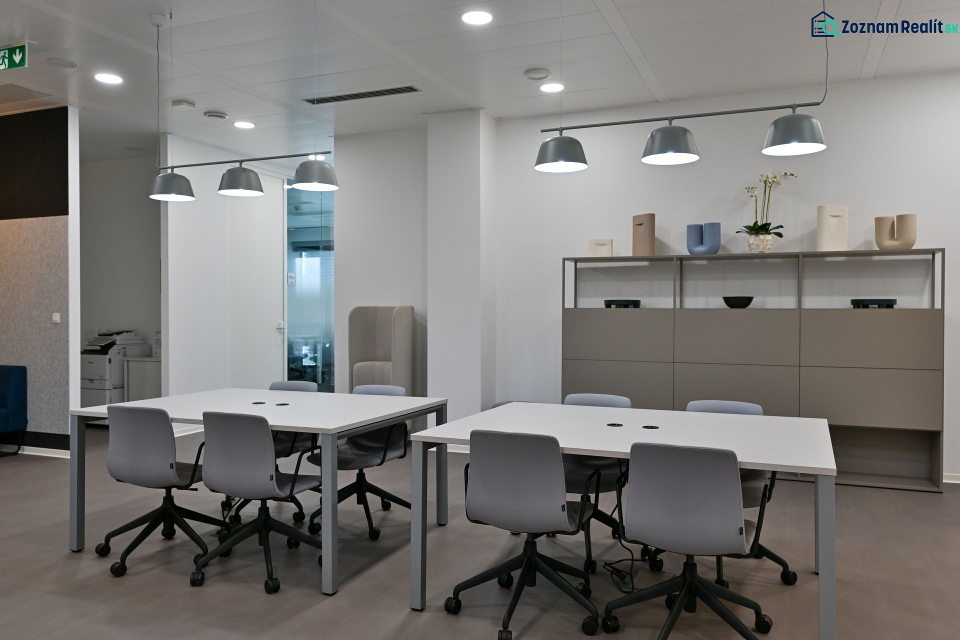 Offices with light gray desks and chairs, pendant lights, shelves with decorations.