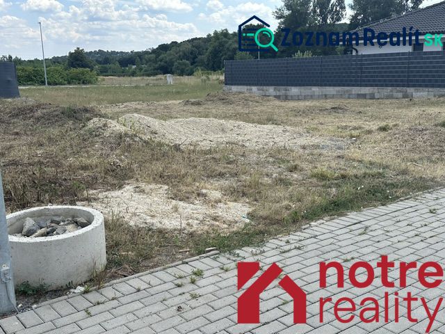 A plot for residential use in Lučenec with a grassy area and a paved walkway on the edge.