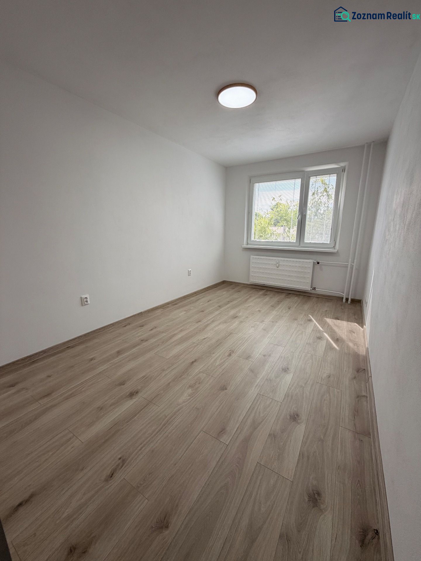 A room with a wooden decor floor in a 2-room apartment, white walls, and a window.