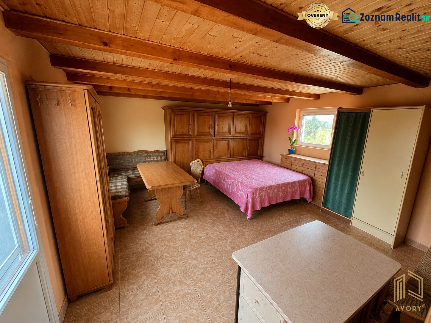 A room in a cottage with a wooden ceiling, a bed, a wardrobe, and a table with chairs.