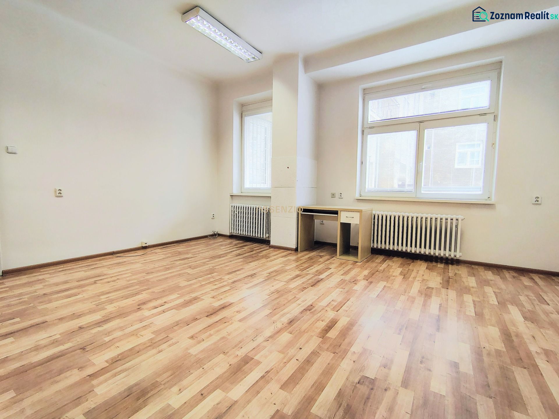 Bright office with wood-patterned flooring, a desk, and white walls.
