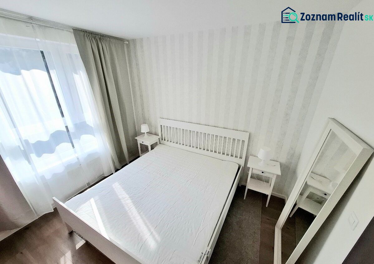 A bright bedroom with a white bed and a wooden decor floor in a 2-room apartment.