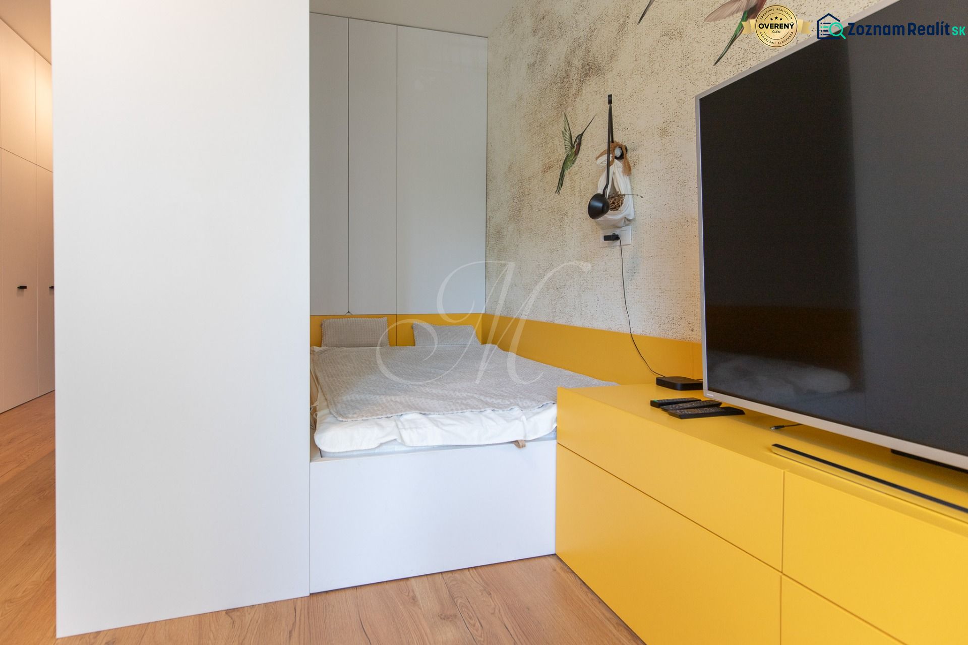 A bedroom in a studio apartment with a bed, TV, and wooden decor flooring.