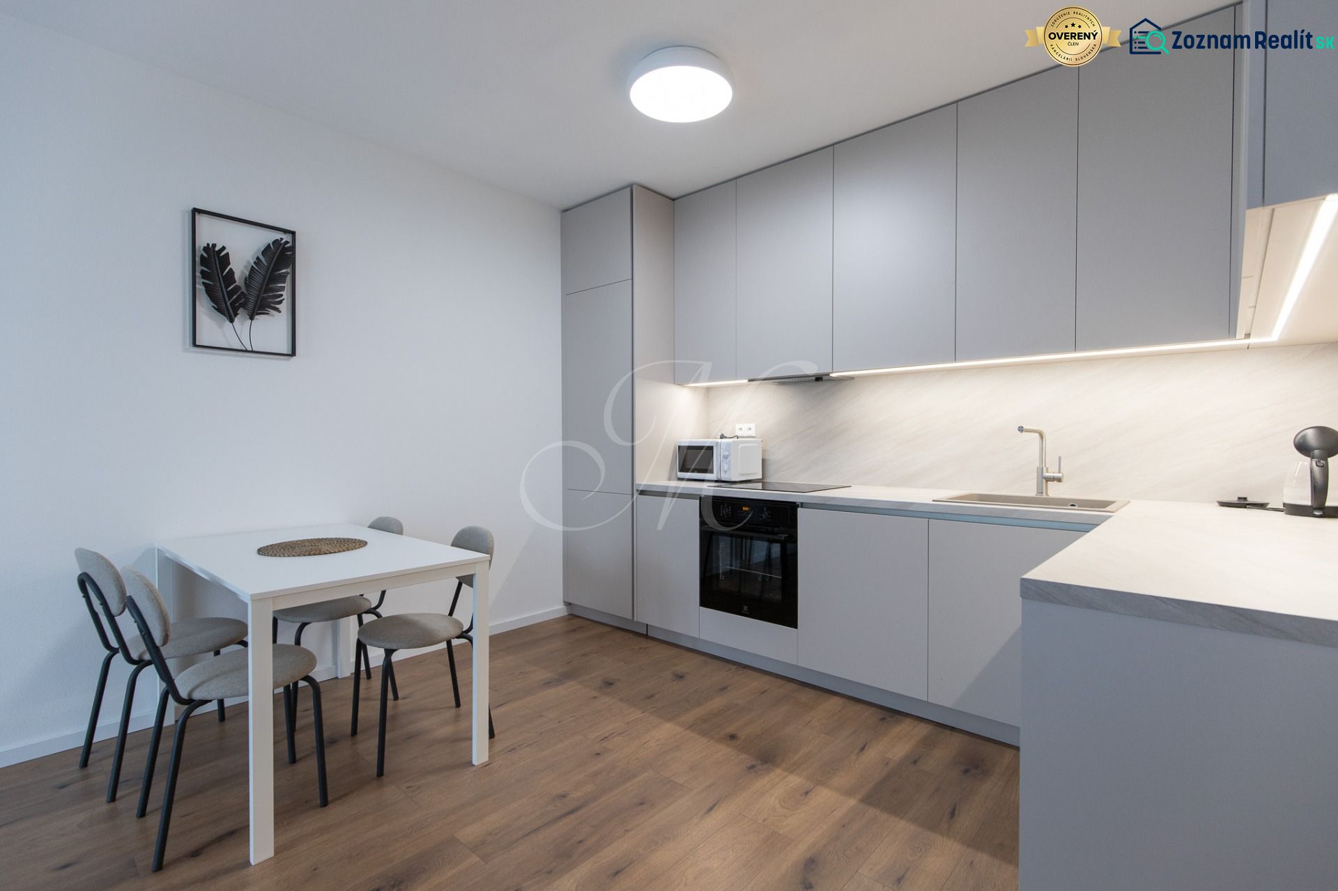 A kitchen in a 2-room apartment with a wooden decor floor, a dining table, and appliances.