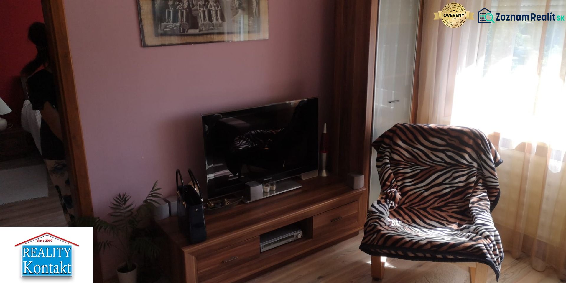 A room with a television, a patterned armchair, and a floor with a wooden decor in a studio apartment.