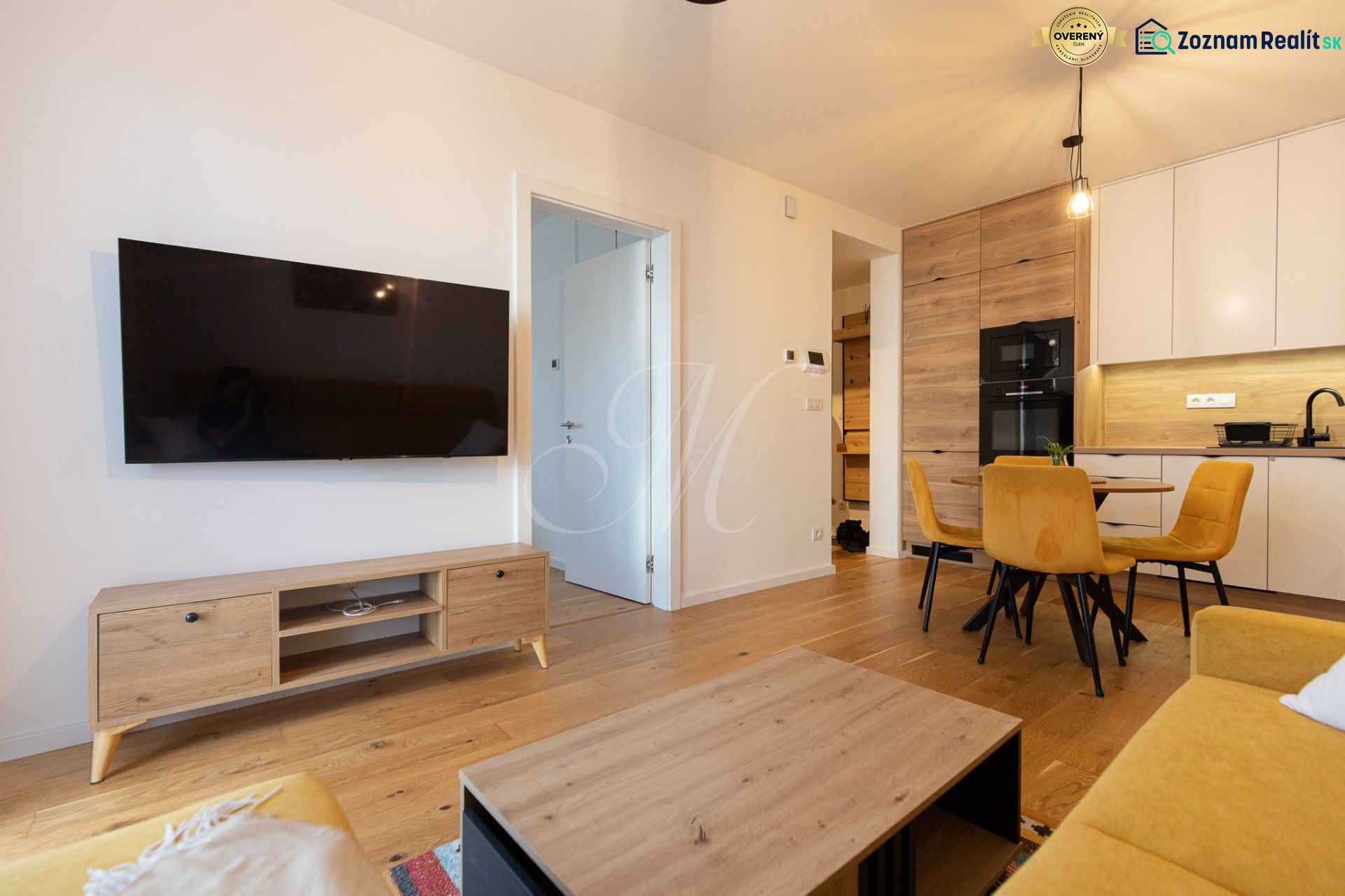 A living room in a two-room apartment with a yellow couch and a wooden decor floor.