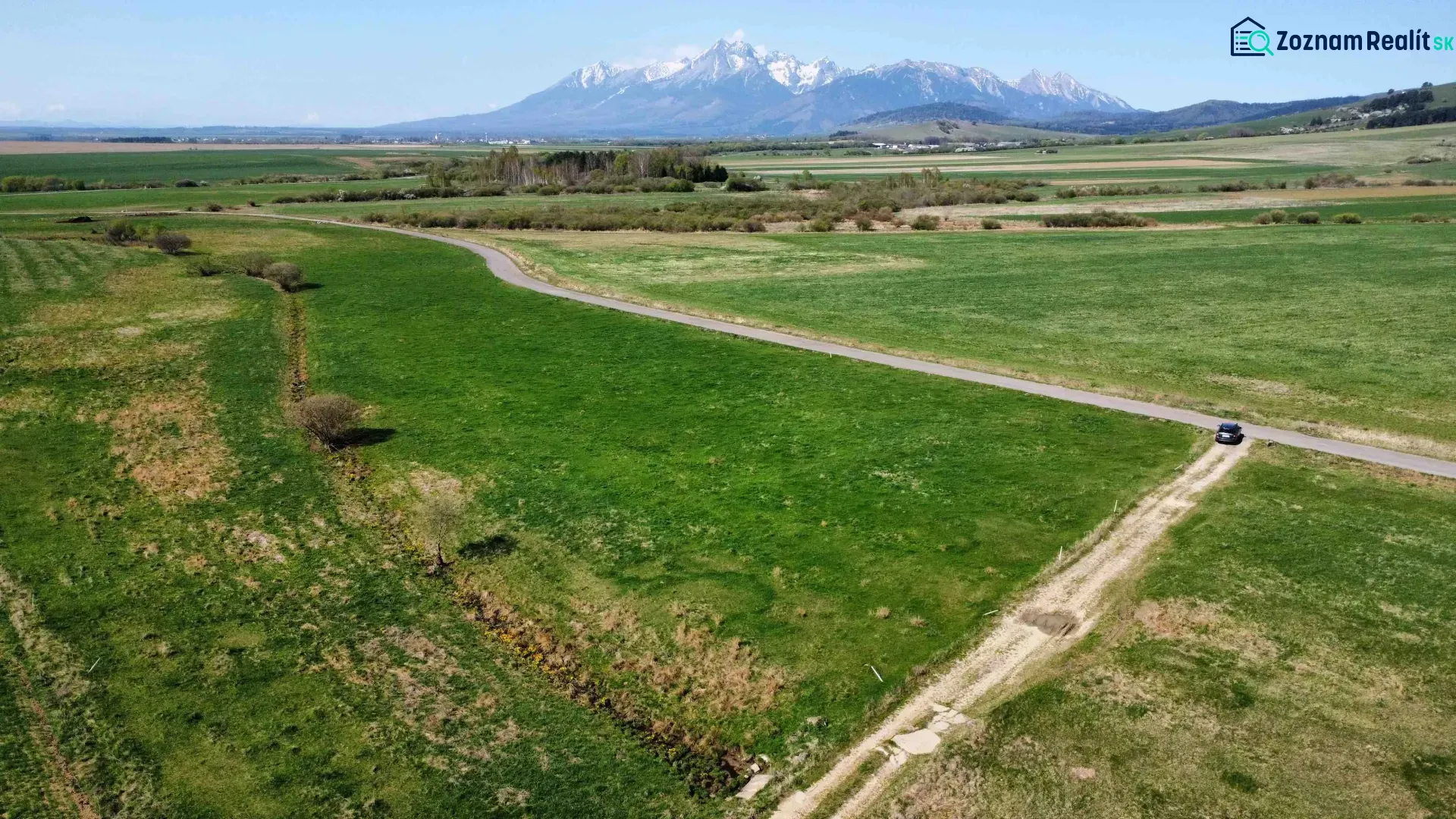 Agricultural and forest lands in Podhorany, with a road and distant mountains on the horizon.