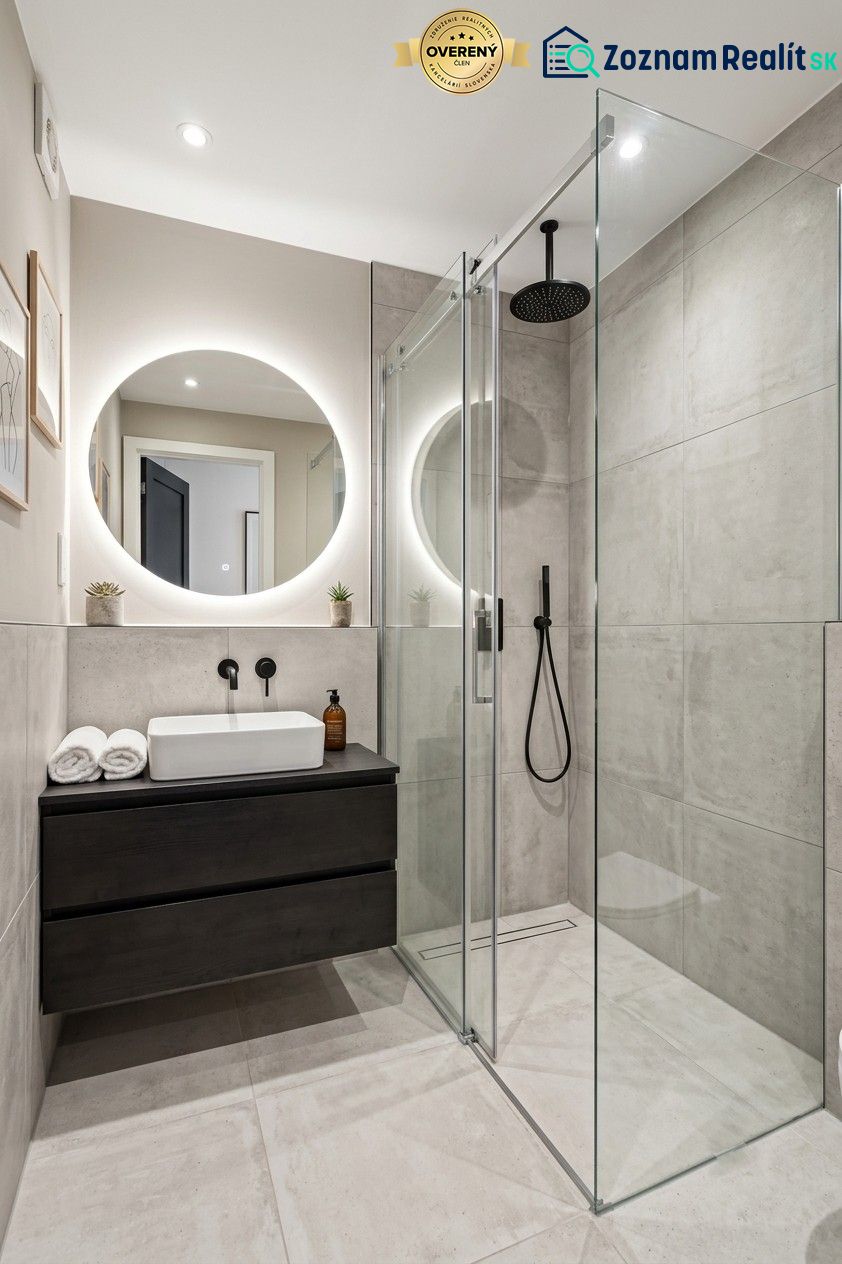 A bathroom in a studio apartment with a modern shower and a round mirror.