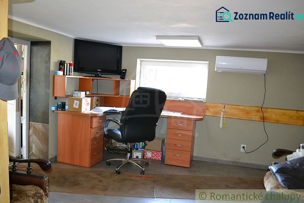 A workspace in a family house with an office desk, shelves, and a television on the wall.