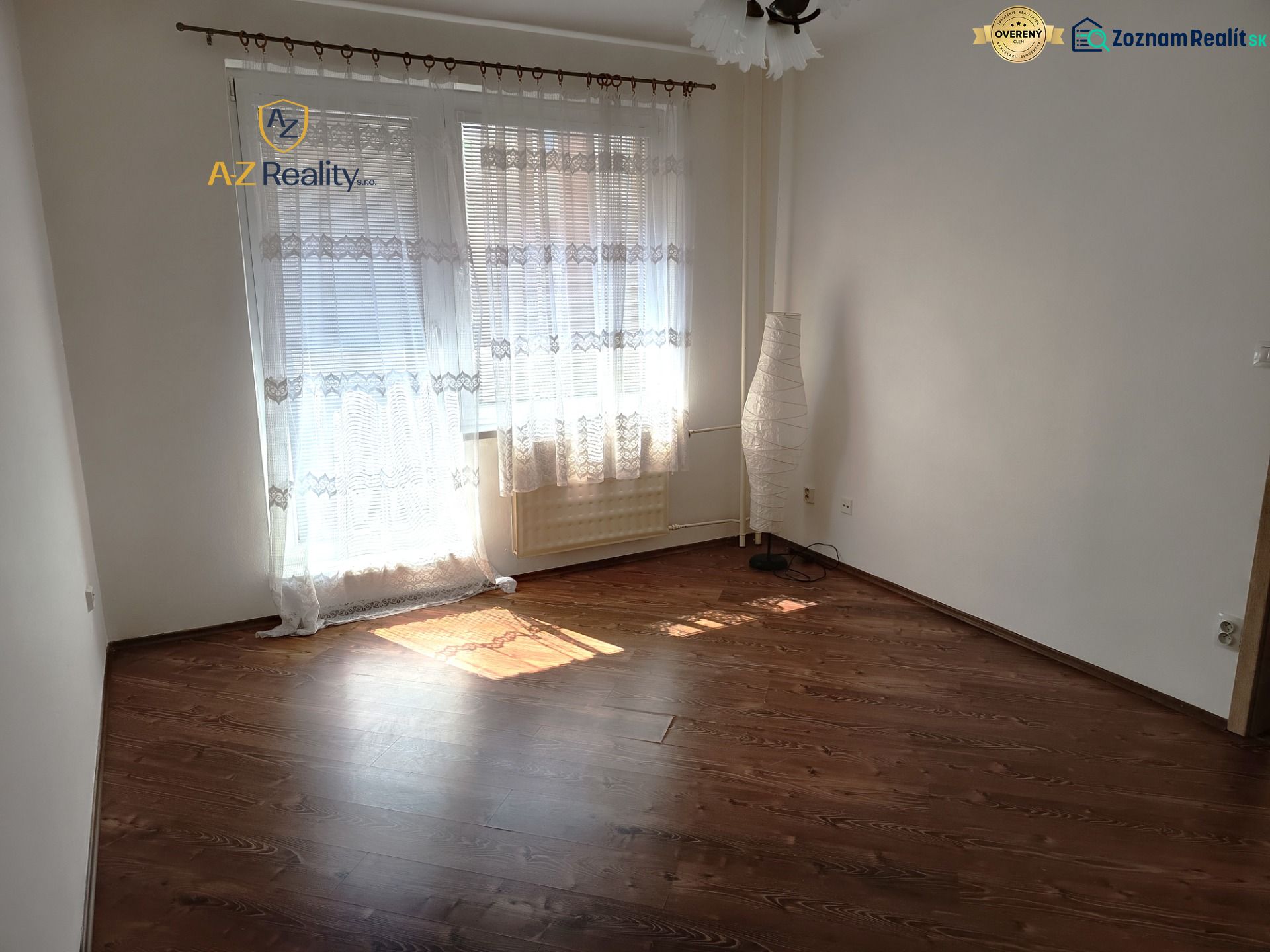 A room in a one-room apartment with a wooden decor floor and curtains.