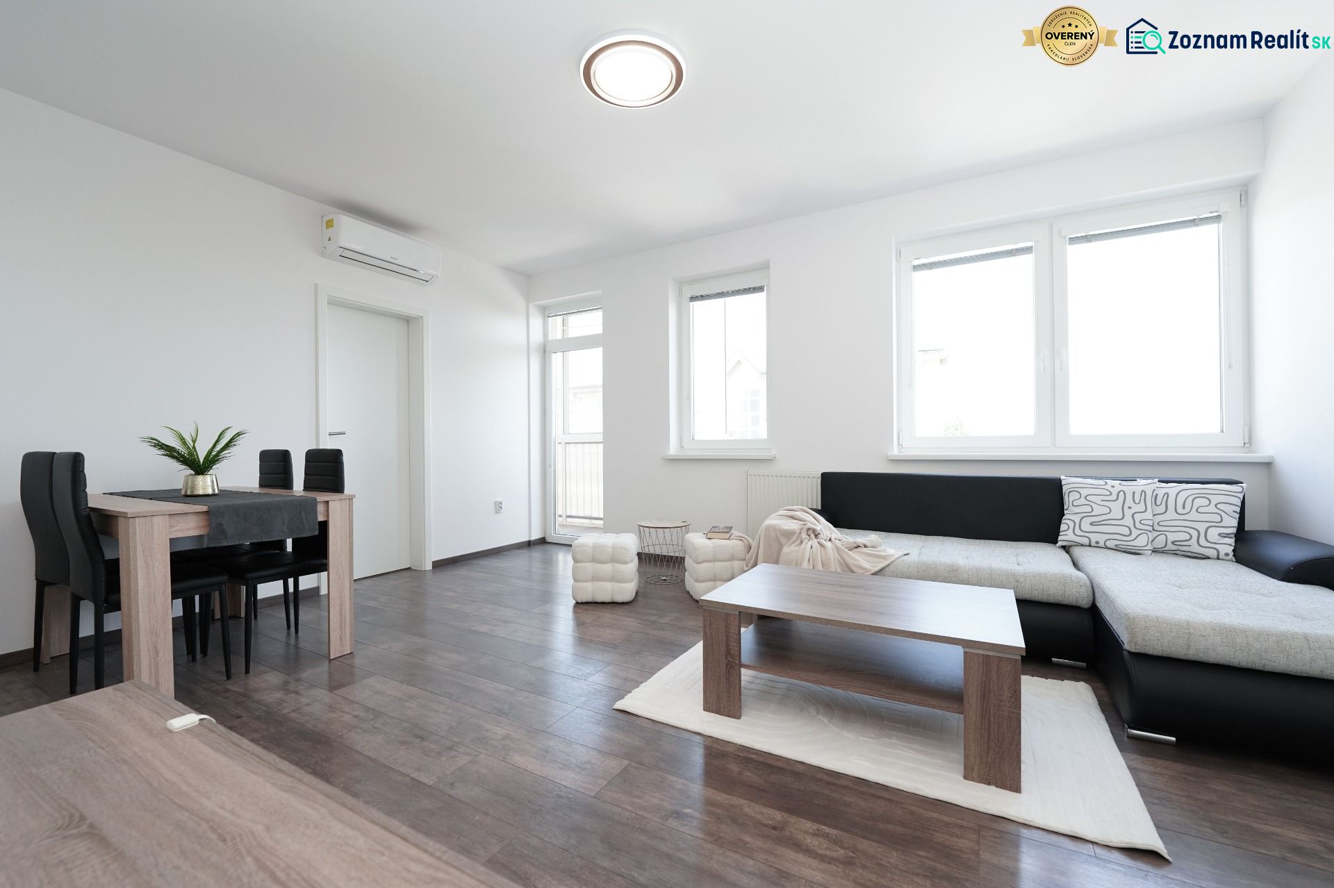 Bright living room with a sofa, dining table, and wood-patterned flooring.