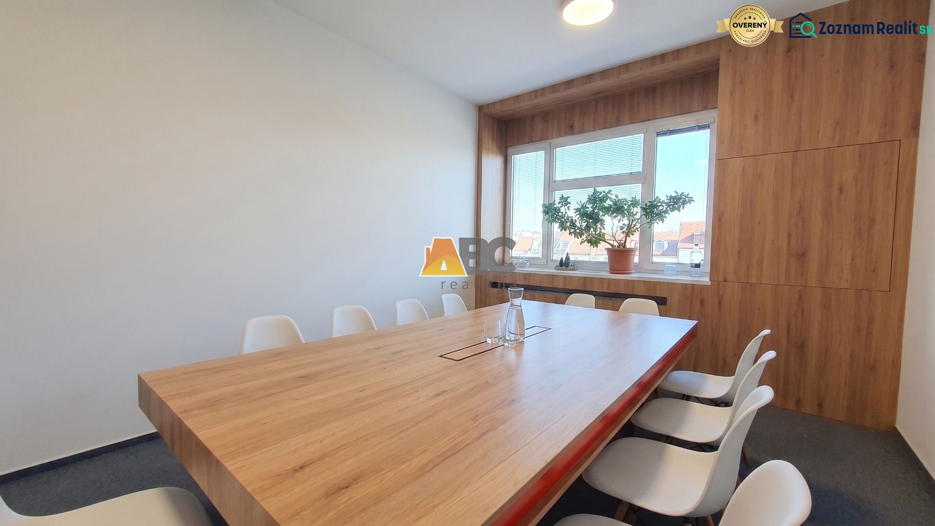 Office with a large table and chairs, floor with wooden decor, window with a plant.