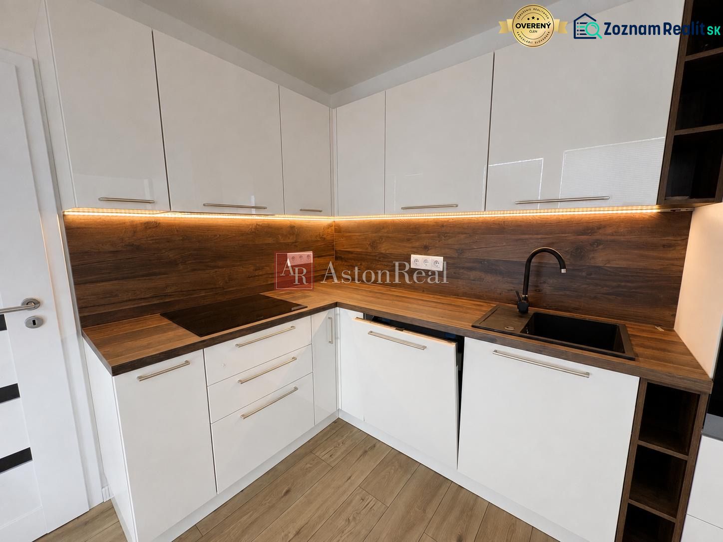 A kitchen in a 2-room apartment with white cabinets and a wooden decor floor.