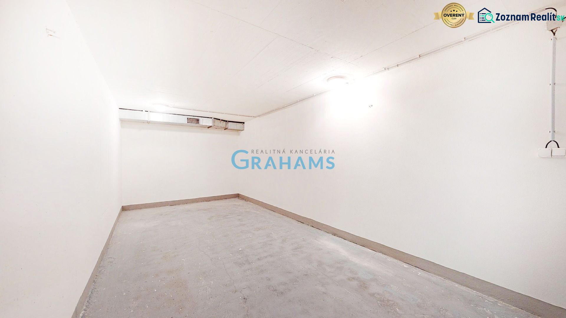 An empty, white interior of garages with a concrete floor and lighting on the walls.