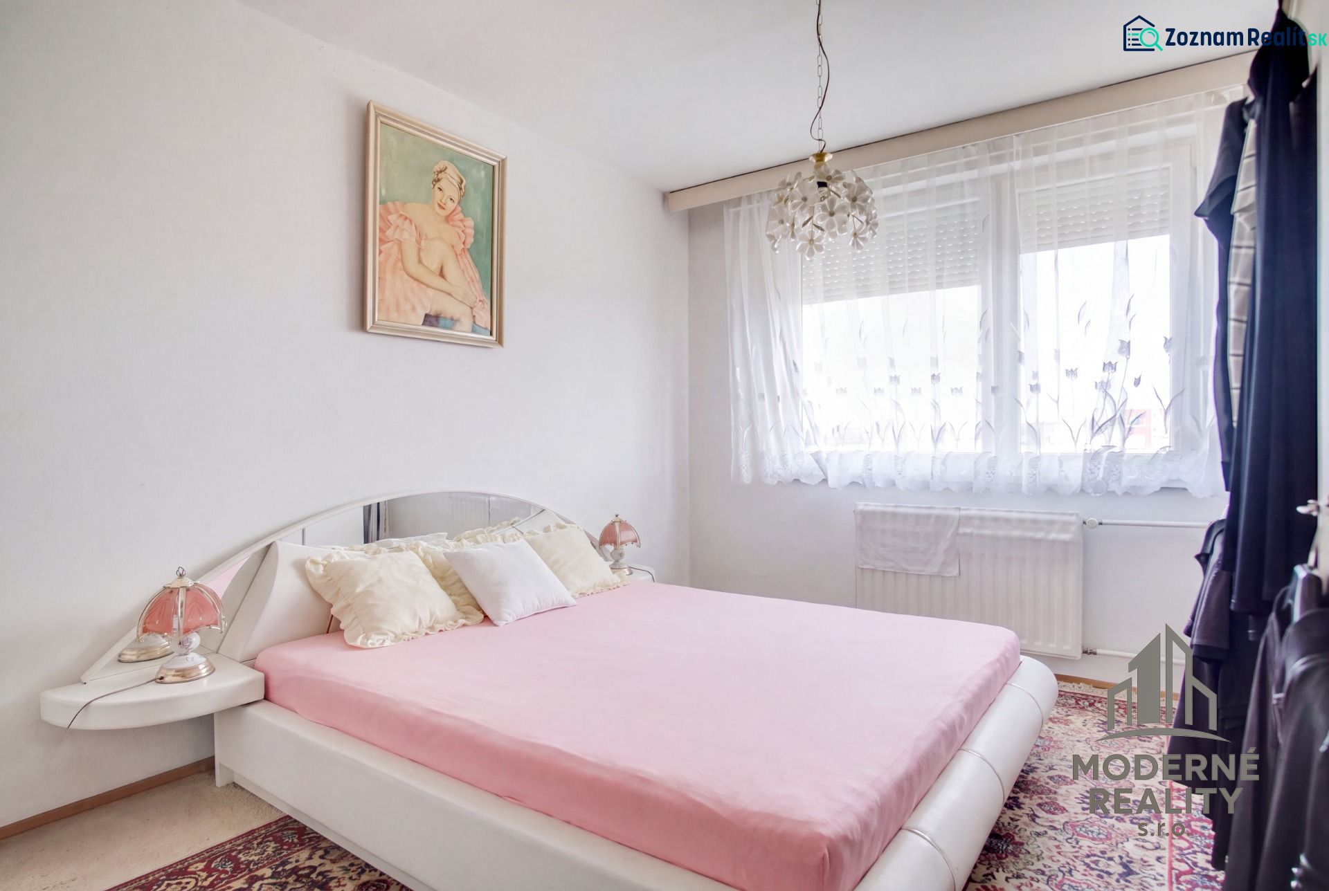 A bedroom in a 4-room apartment with white walls, a decorative carpet, and a bed.