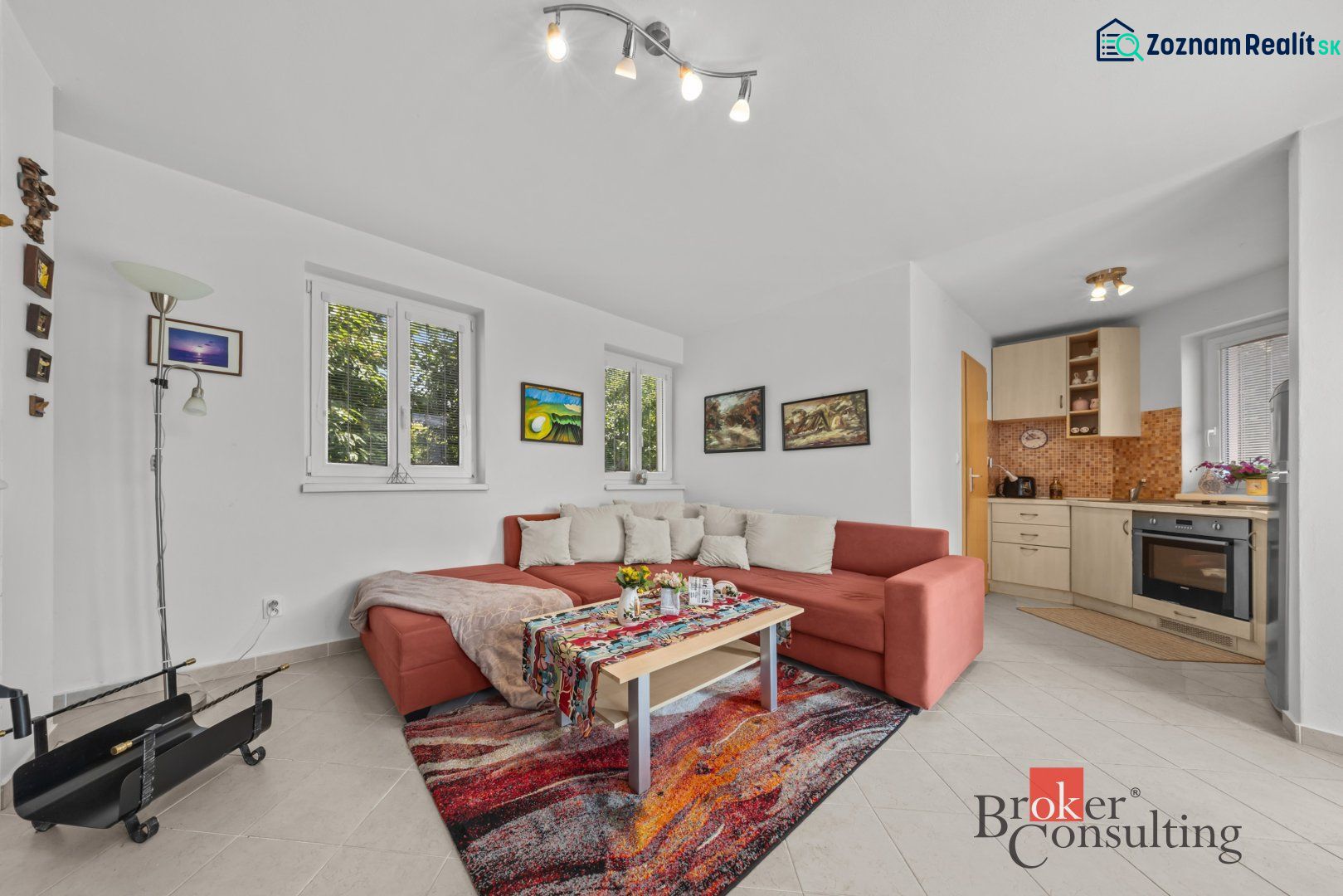 Living room with a red sofa, colorful carpet, and kitchenette in a cottage.