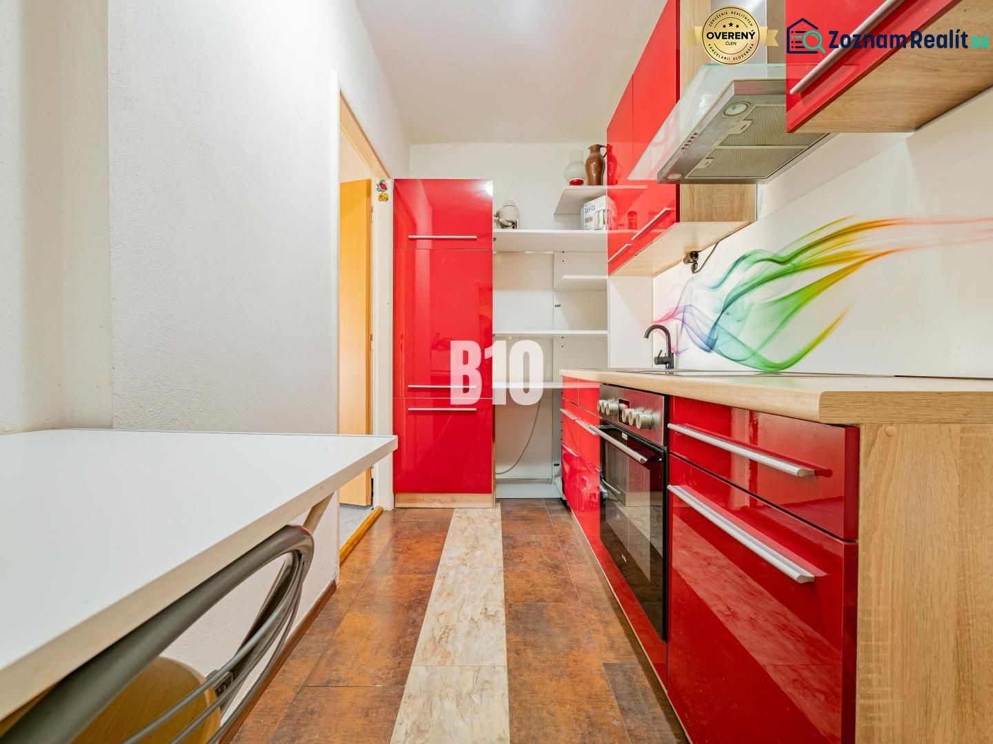A kitchen in a 3-room apartment with vibrant red cabinets and a wood-patterned floor.