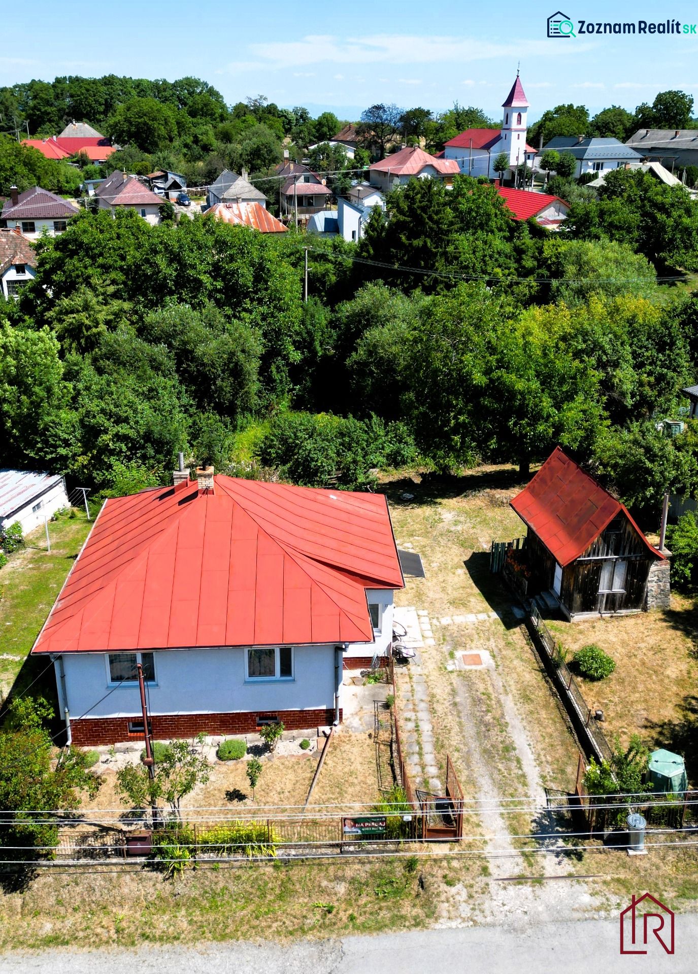 A family house in the village of Slanská Huta with a red roof surrounded by greenery.