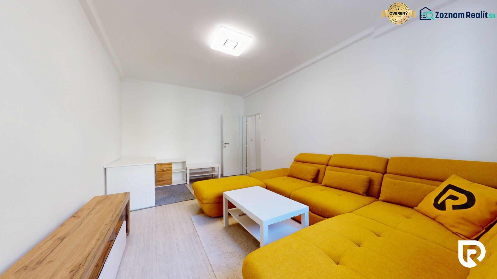 Living room of a two-room apartment with a yellow sofa and a white table.