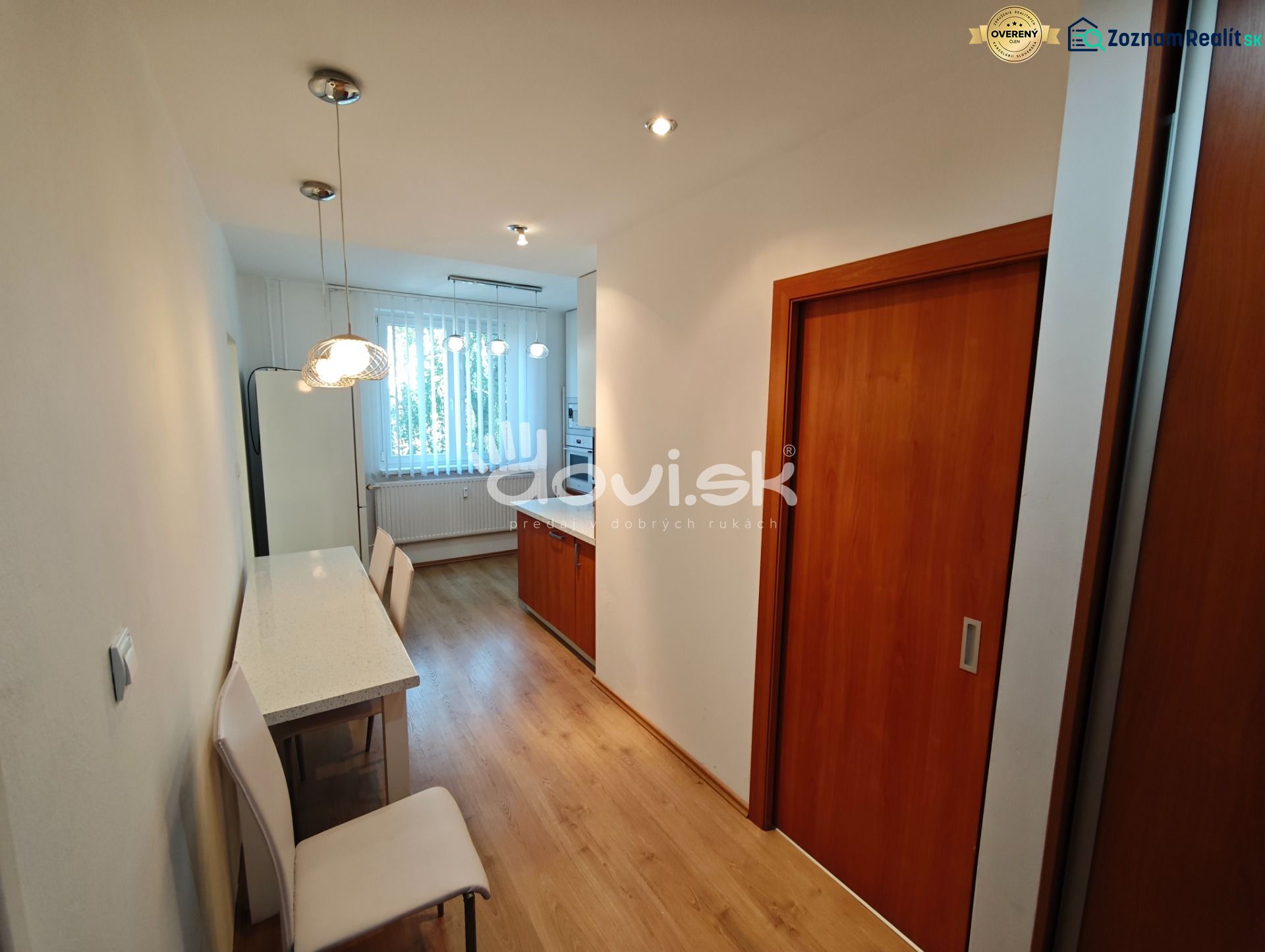 A kitchen in a one-room apartment with a wooden decor floor and a white table.