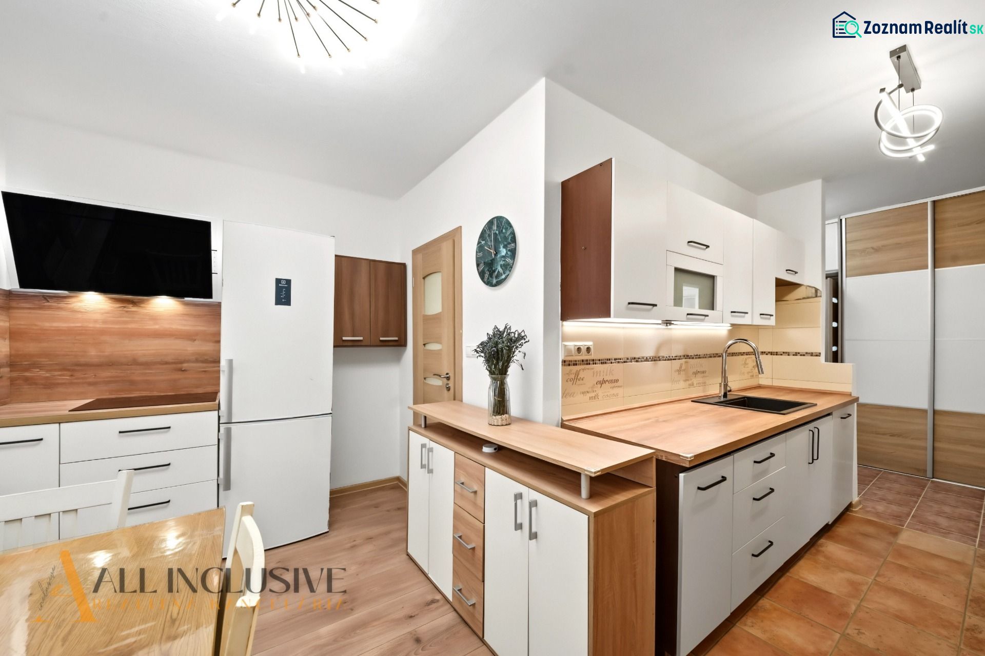 A kitchen in a 2-room apartment with a white refrigerator, wooden decor on the floor and walls.