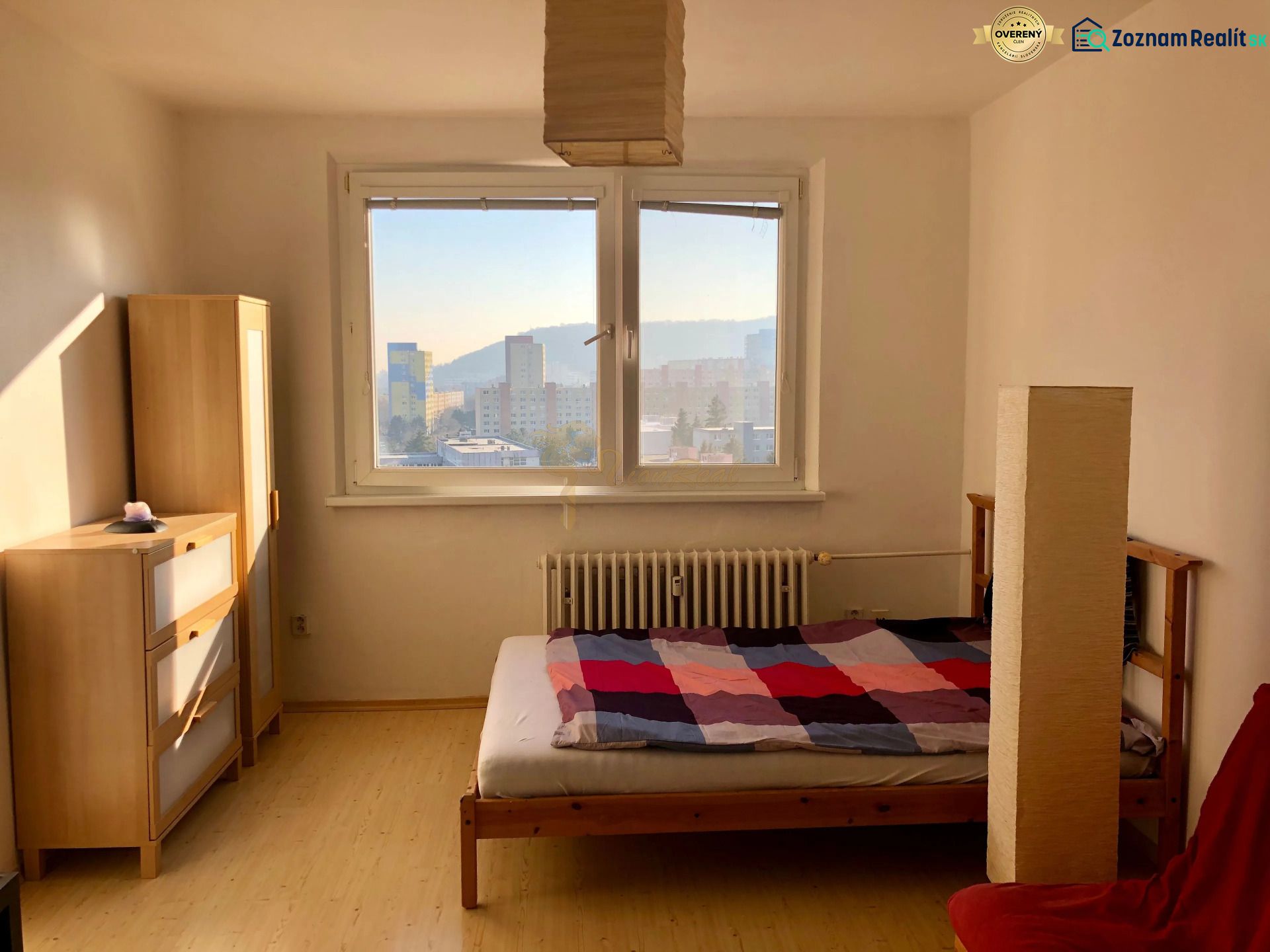 A bedroom in a studio apartment with a bed, a cabinet, and a floor with a wooden decor.
