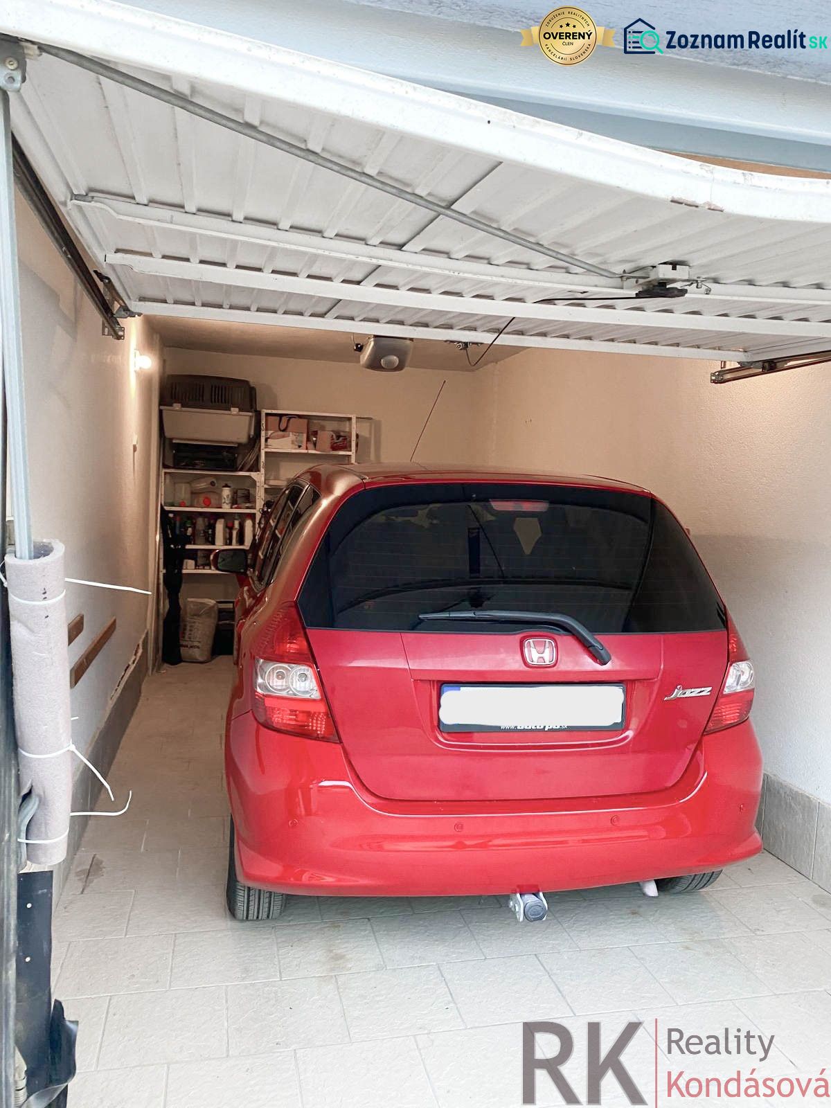 A red car parked in a garage with shelves on the wall, tiled floor.