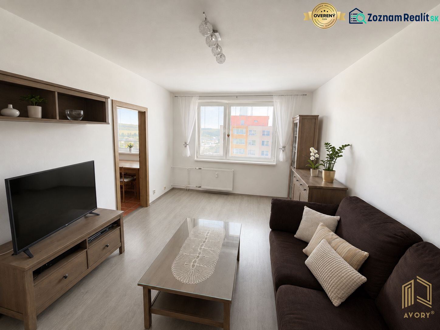 A living room in a three-room apartment with a wooden decor floor and a dark sofa.