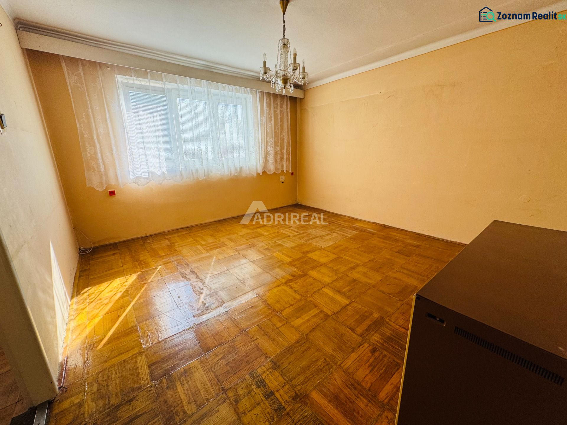 A room in a 2-room apartment with a crystal chandelier and a wooden decor floor.