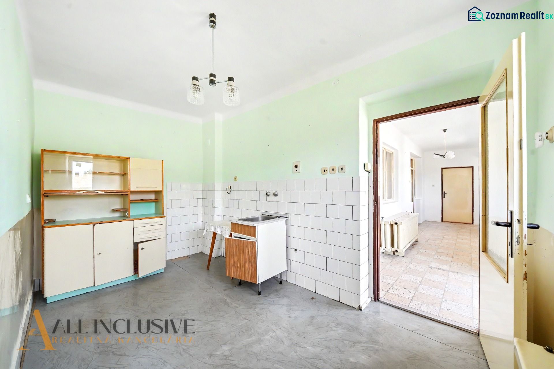 A kitchen in a family house with a simple kitchen unit, white tiles, and a gray floor.