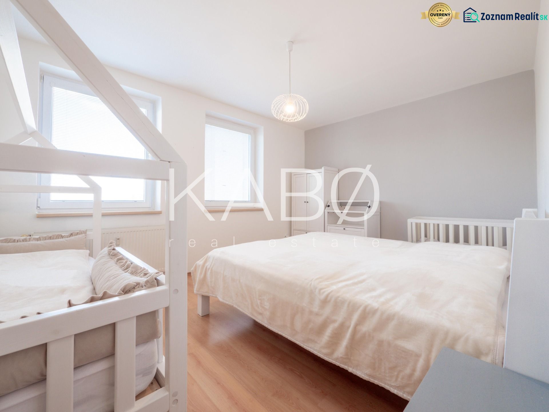 A bright bedroom in a two-room apartment with a bed, a baby crib, and a wooden decor floor.
