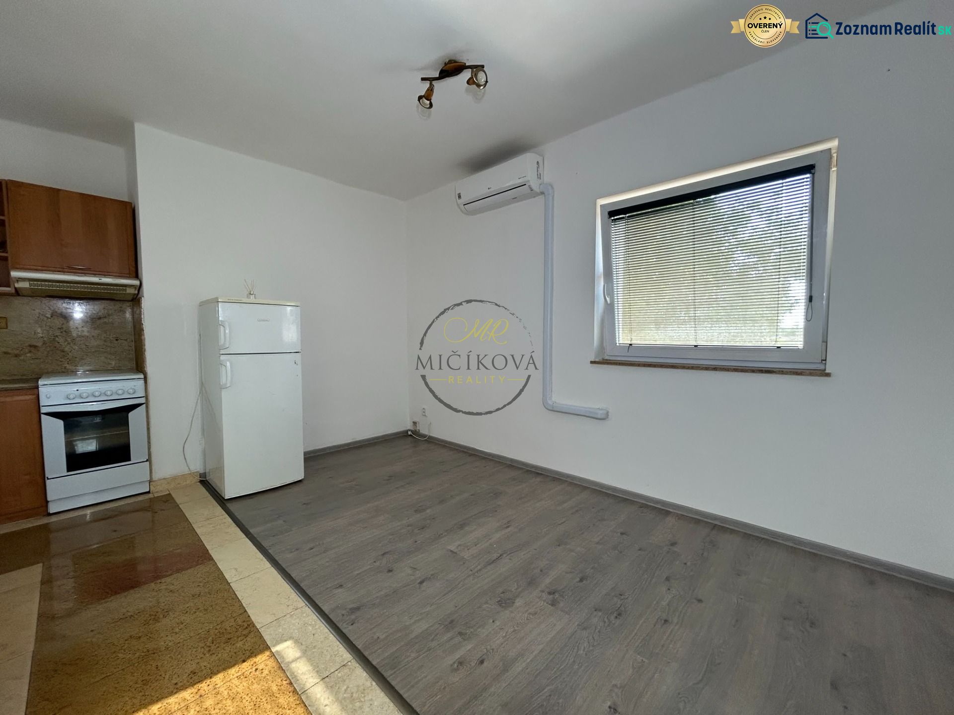 A kitchen in a 2-room apartment with a wooden decor floor, a white refrigerator, and a stove.