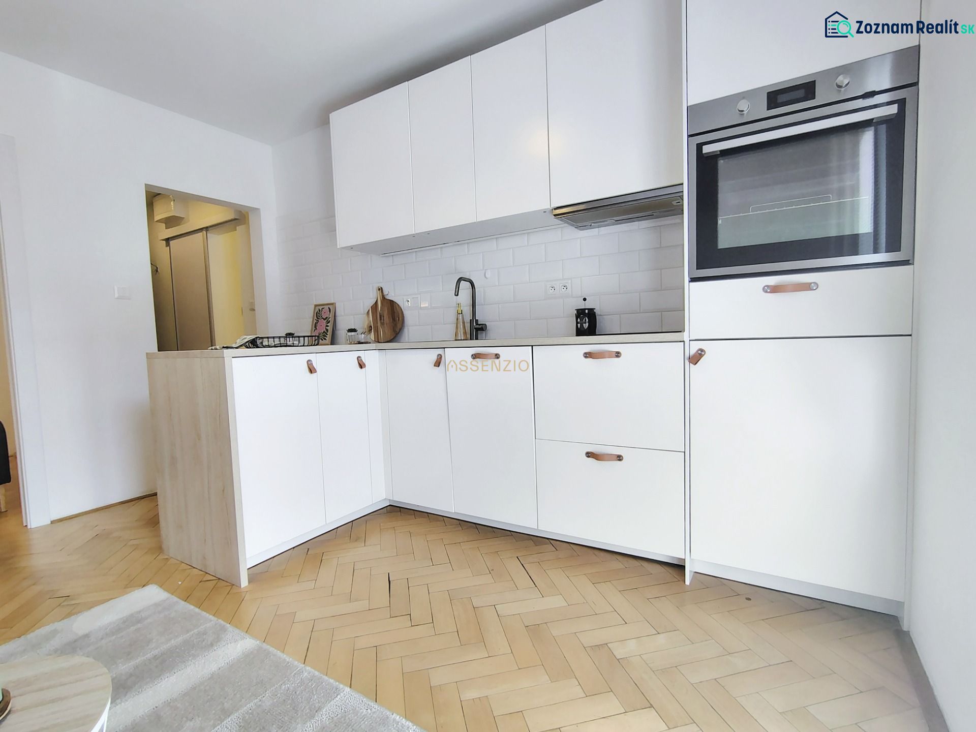 A kitchen in a 2-room apartment with light cabinets and a wooden decor floor.