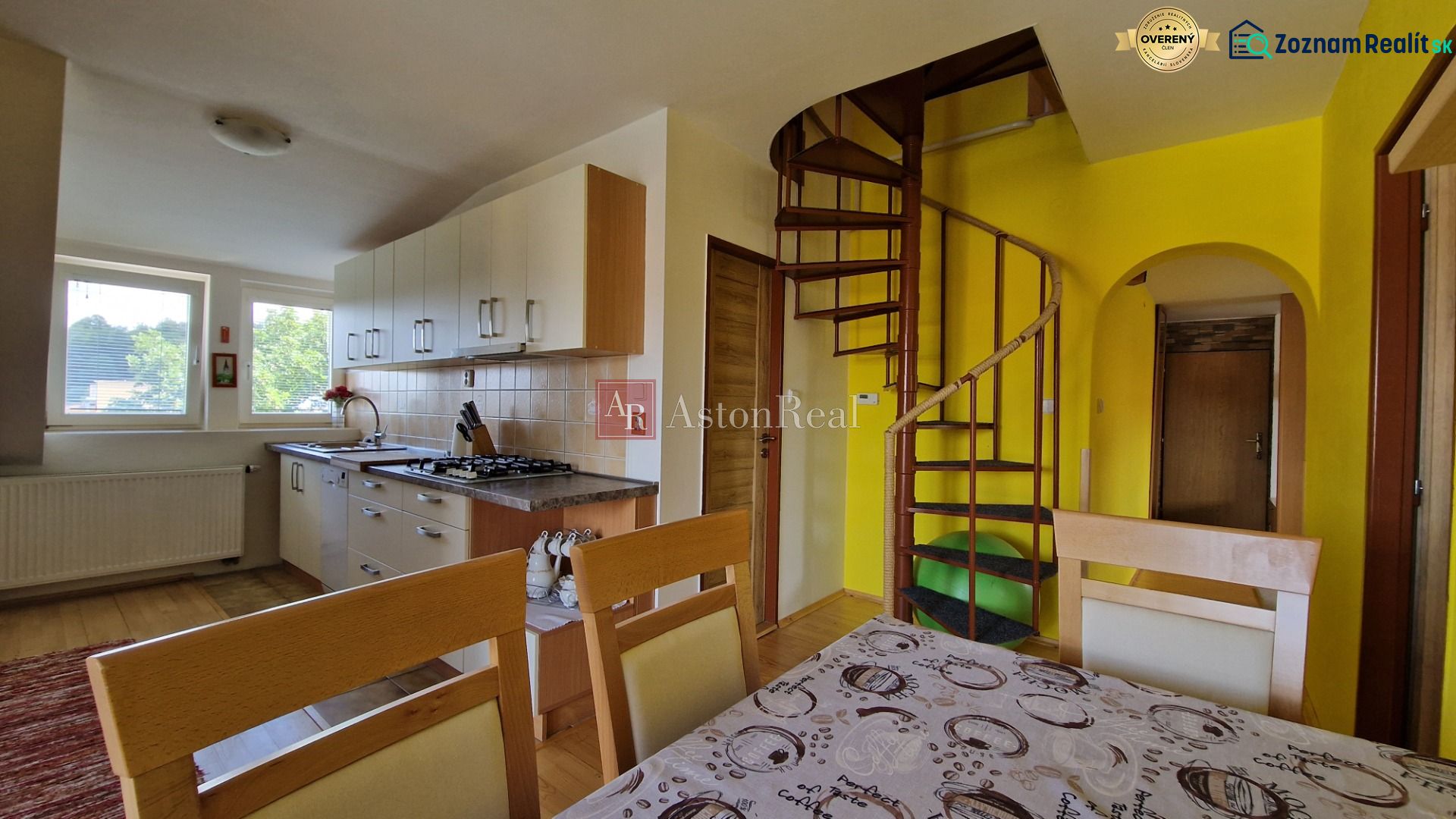 A kitchen in a 2-room apartment with a spiral staircase and light cabinets.