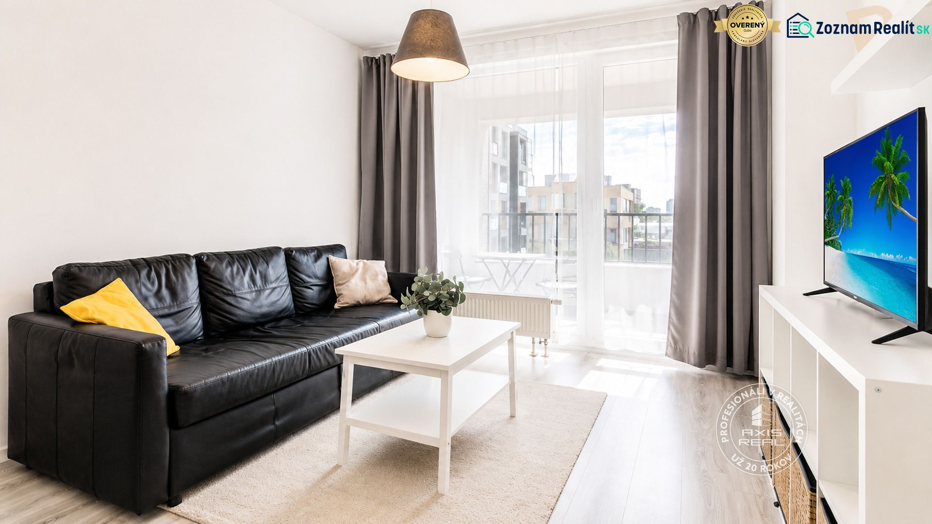 Living room in a two-room apartment with a black sofa and a white table.